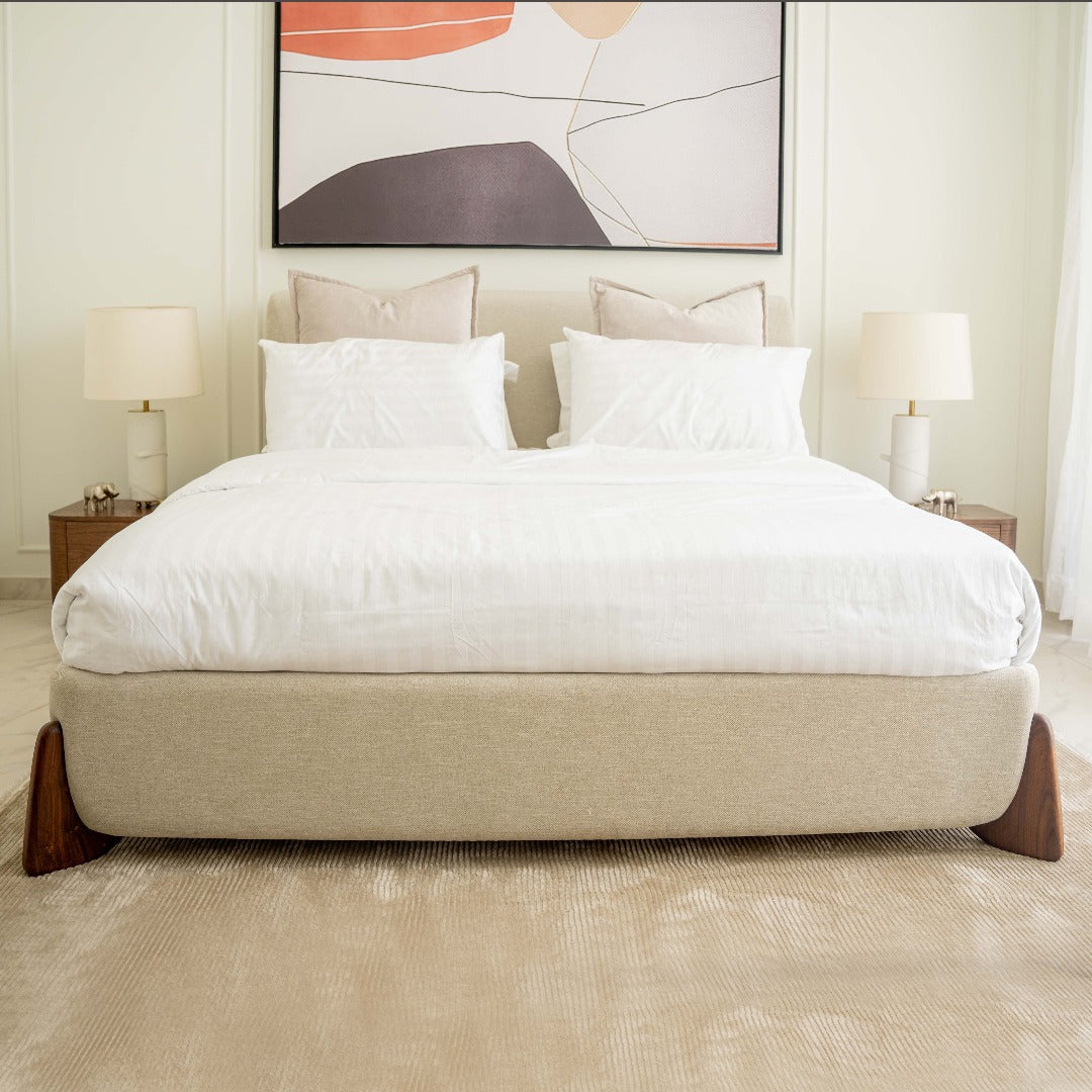A bed featuring a unique boomerang-style Indian rosewood leg detail, adding a touch of exotic elegance to its design. The rich wood grain and distinctive shape of the legs create a striking visual contrast, enhancing the aesthetic appeal of the bed.