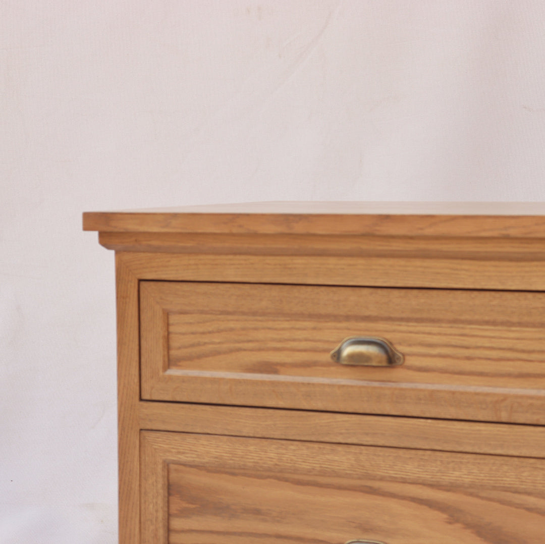 "Classic wooden bedside table with two spacious drawers, crafted from natural wood with a rich grain finish and antique brass handles. Perfect for adding timeless elegance and functional storage to your bedroom."